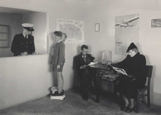 Weighing in for a Palestine Airways flight, February 1939. Imperial Airways crew piloted and serviced the aircraft and handled passenger check-in. Posters of Imperial Airways and Palestine Airways decorate the wall, and a KLM poster is on the table. (Israel Government Press Office) 