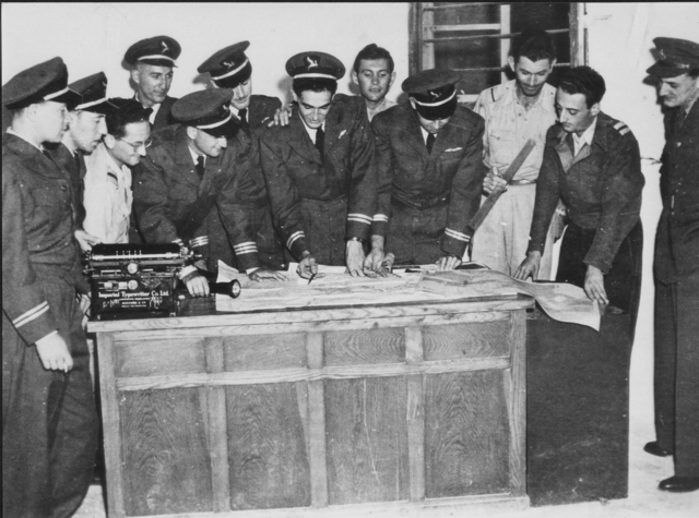 Meteorological briefing at Ekron Air Base, 28 September 1948, prior to takeoff on the first "EL AL" flight, to pick up Chaim Weizmann in Geneva. Left to right: Yitzhak Hennenson (co-captain); Joe Segal (radio operator); ground staff member; Sy Cohen (navigator); Hal Auerbach (co-captain); Arnold Ilowite (co-captain); Abie Nathan (second officer) (in center pointing with pen); tower operator; crew member [Yehuda Shimoni?]; ground staff member; meteorologist [Fayge?]; military representative. (State of Israel Ministry of Defence, Military (I.D.F.) & Defence Establishment Archives)