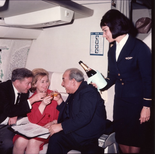 Enjoying Champagne aboard an EL AL 707 are performers of Israel's national theatre, Habima, including at left Shmuel Segal and at right Shmuel Rodenski, being served by flight attendant Judy Amir. EL AL originally decorated the side panels of its 707 cabins, as here, with artwork by Israeli artist Jean David, and continued the handsome Britannia-era uniforms into this 1960s early jet period. (EL AL)